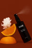 Black face mist spray bottle with orange slices and white flowers on a red background