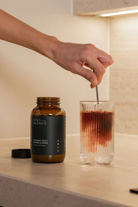 Person stirring a drink in a glass with a bottle labeled 'BIO BLANDS' on a countertop.