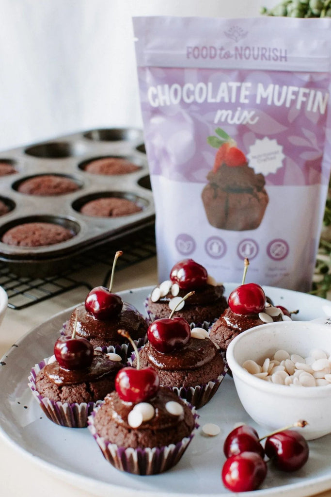 Chocolate muffins with cherries on a plate next to a bag of chocolate muffin mix.