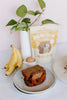 Two slices of banana bread on a plate with a package of banana bread mix, bananas, and an egg in the background.
