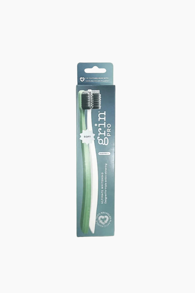 A packaged toothbrush with white bristles and a green and white handle, labeled 