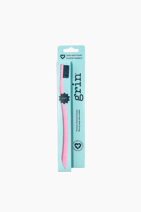A soft toothbrush with pink and black bristles on a recycled cardboard backing card, with a label that says 'grin'.