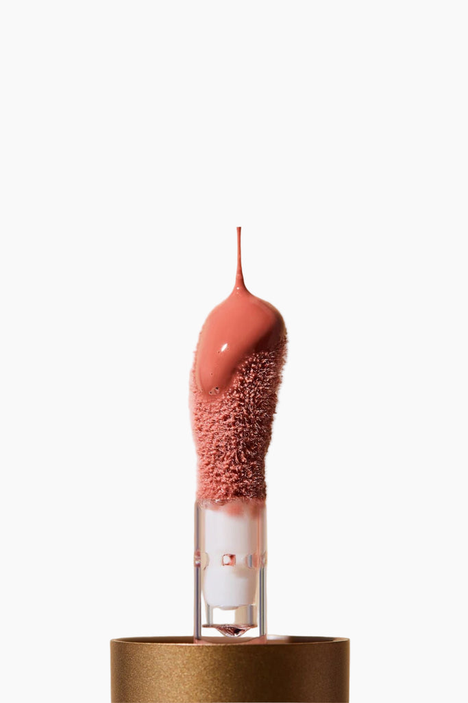Makeup brush with pink bristles and pink liquid on a beige background
