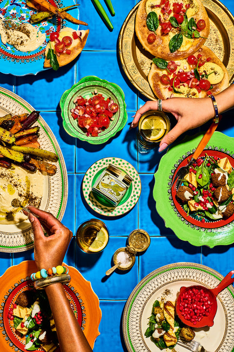 Colorful dining scene with plates of food and hands interacting on a blue tiled table.