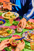 People enjoying a meal with various dishes and drinks on a colorful tablecloth.