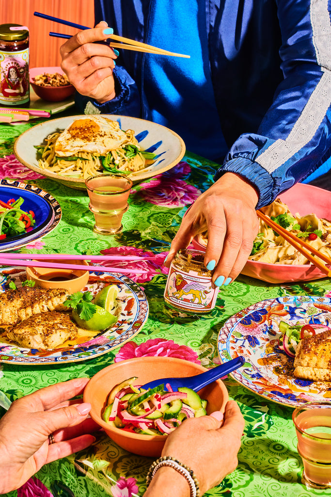 People enjoying a meal with various dishes and drinks on a colorful tablecloth.