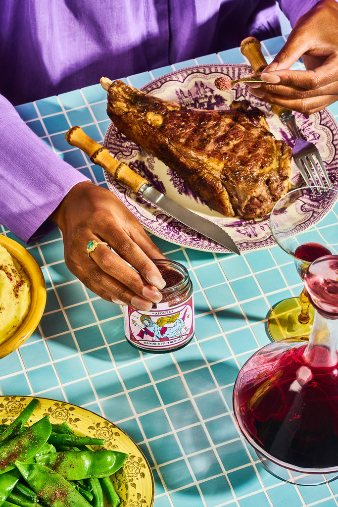 Person at a dining table with a plate of food, a jar of jam, and a glass of red wine.