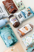 Assorted health and wellness products including a bottle, jars, and packaged snacks on a light background.