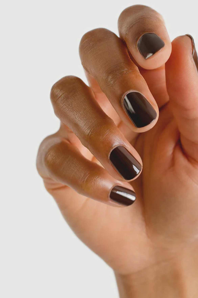 Close-up of a hand with dark brown nail polish on a light gray background
